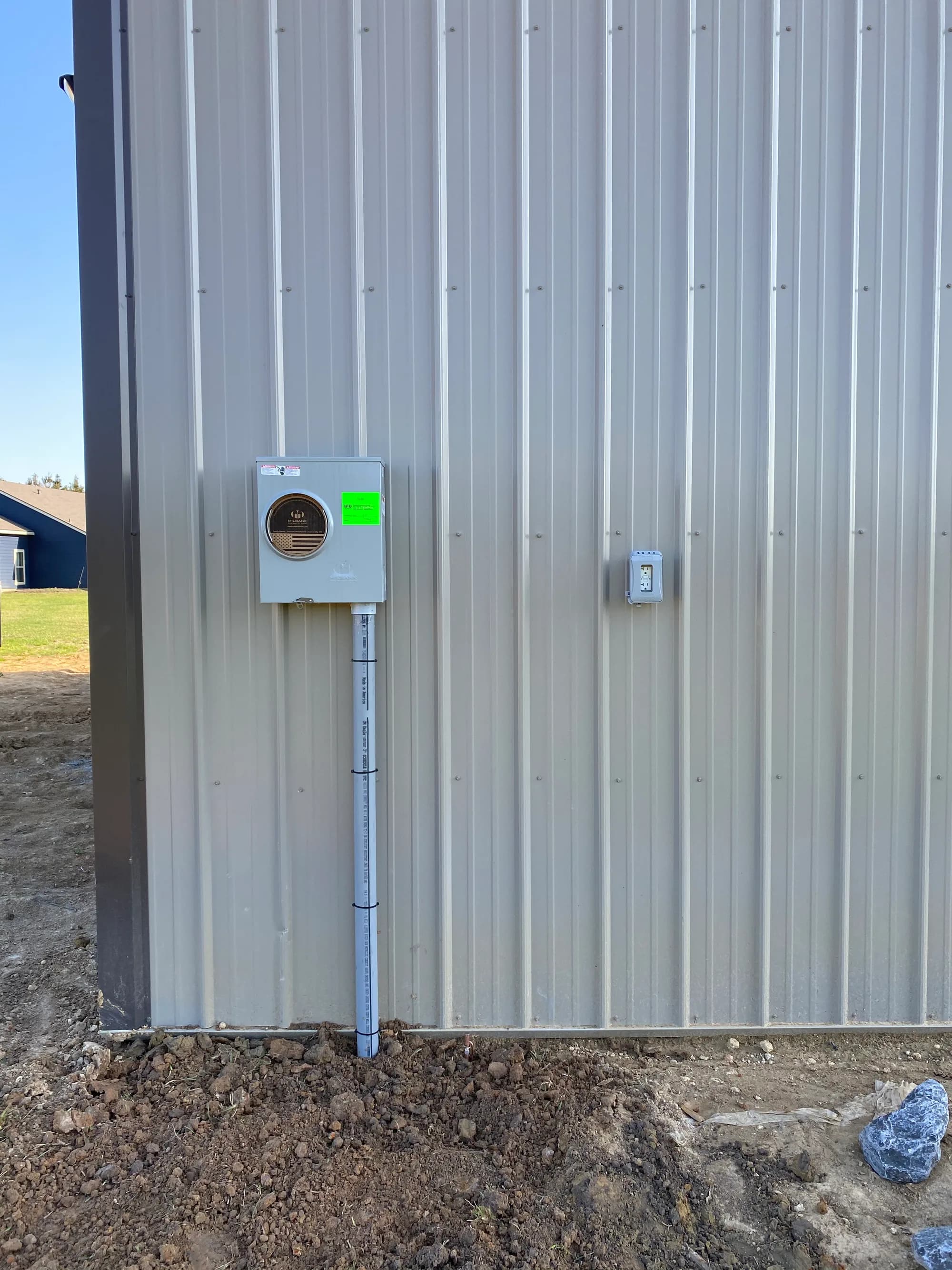 Service disconnect mounted on the metal-siding shop exterior with conduit running down to the trench